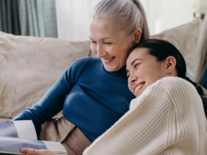 Older woman and her adult daughter laughing together on a sofa at home