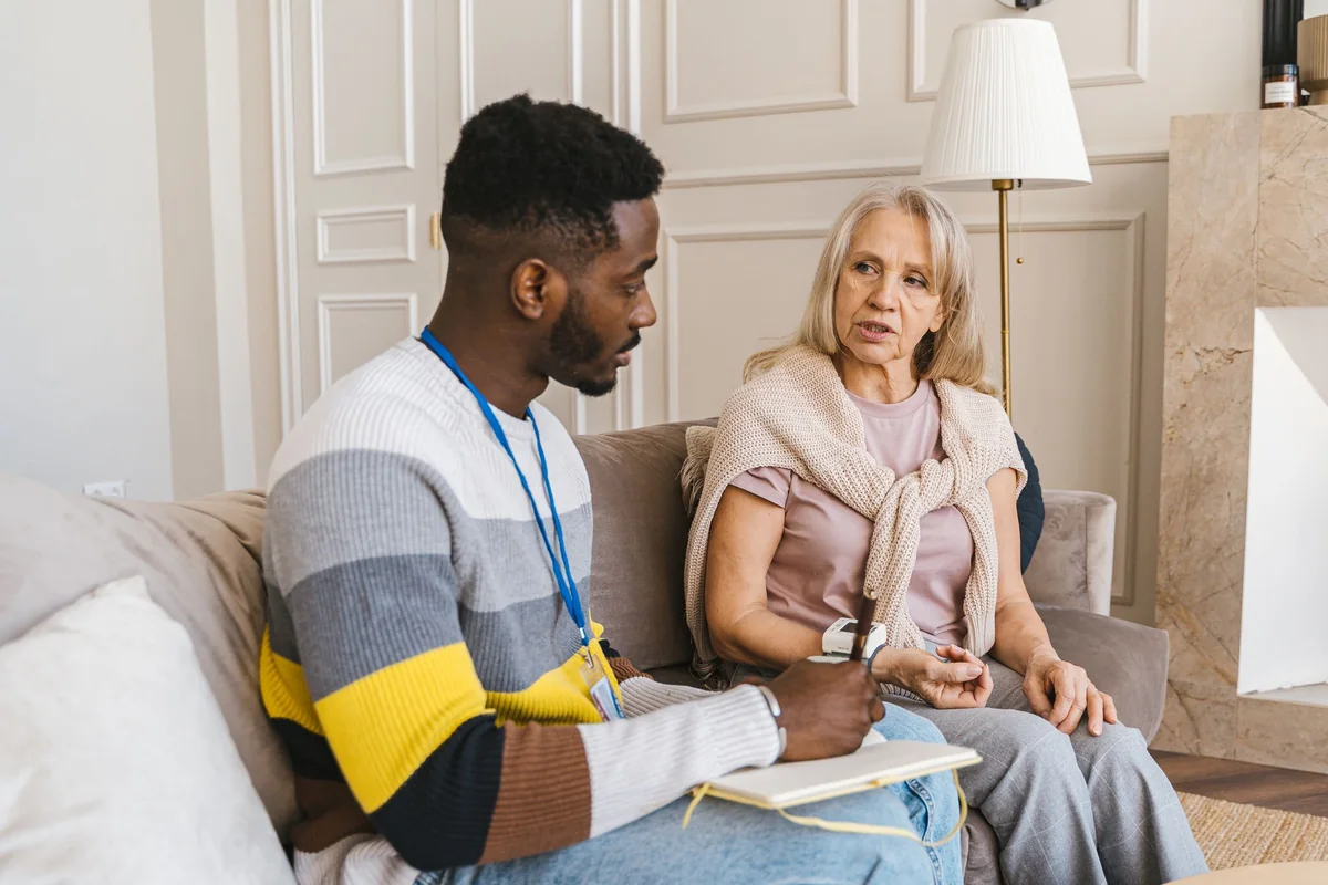 Care coordinator taking notes while talking with an older woman in her living room
