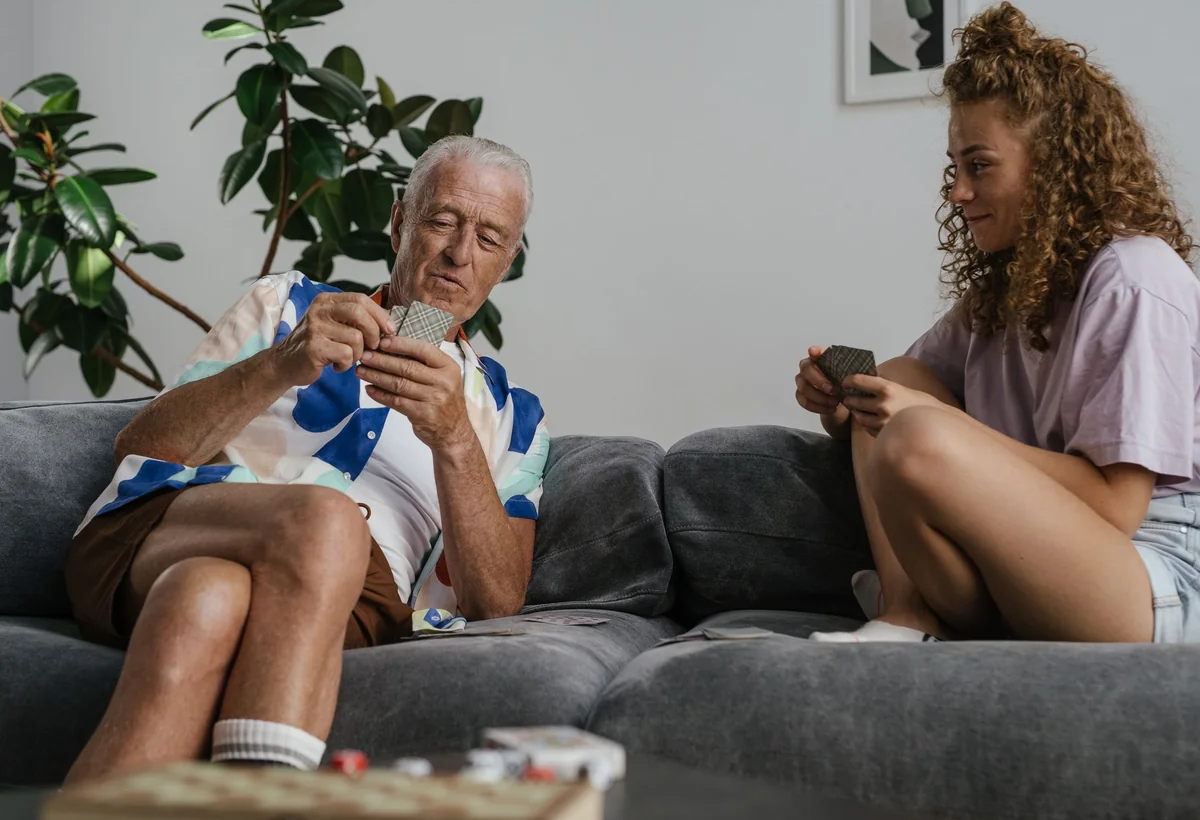 Older man and young woman playing cards together on a sofa at home