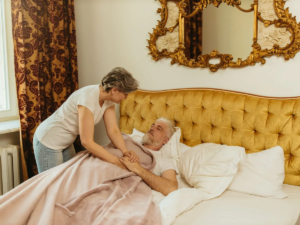 Carer holding an older man's hand as she settles him into bed at home