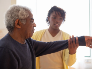 Carer supporting an older man through gentle arm exercises at home